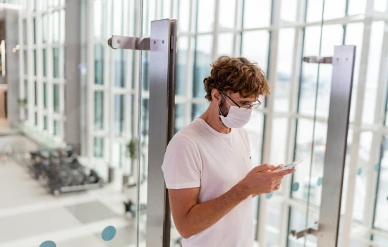 man-wearing-face-mask-in-airport-and-using-smartphone-for-gp-consult-travel-cancellation
