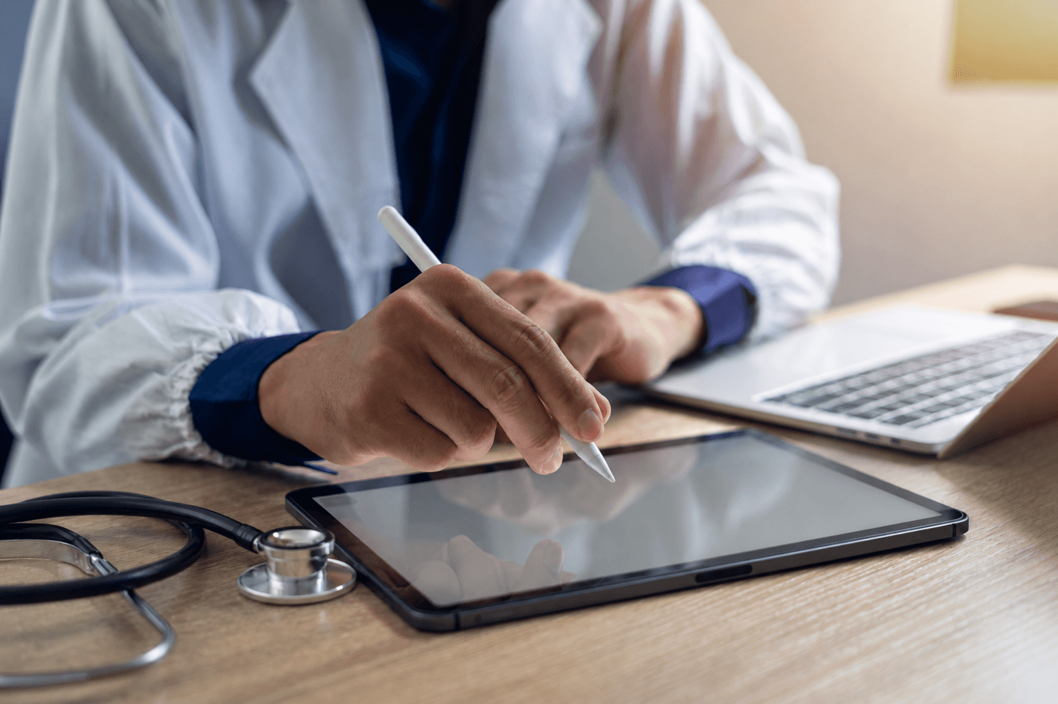 Online GP with a tablet and laptop writing a sick note